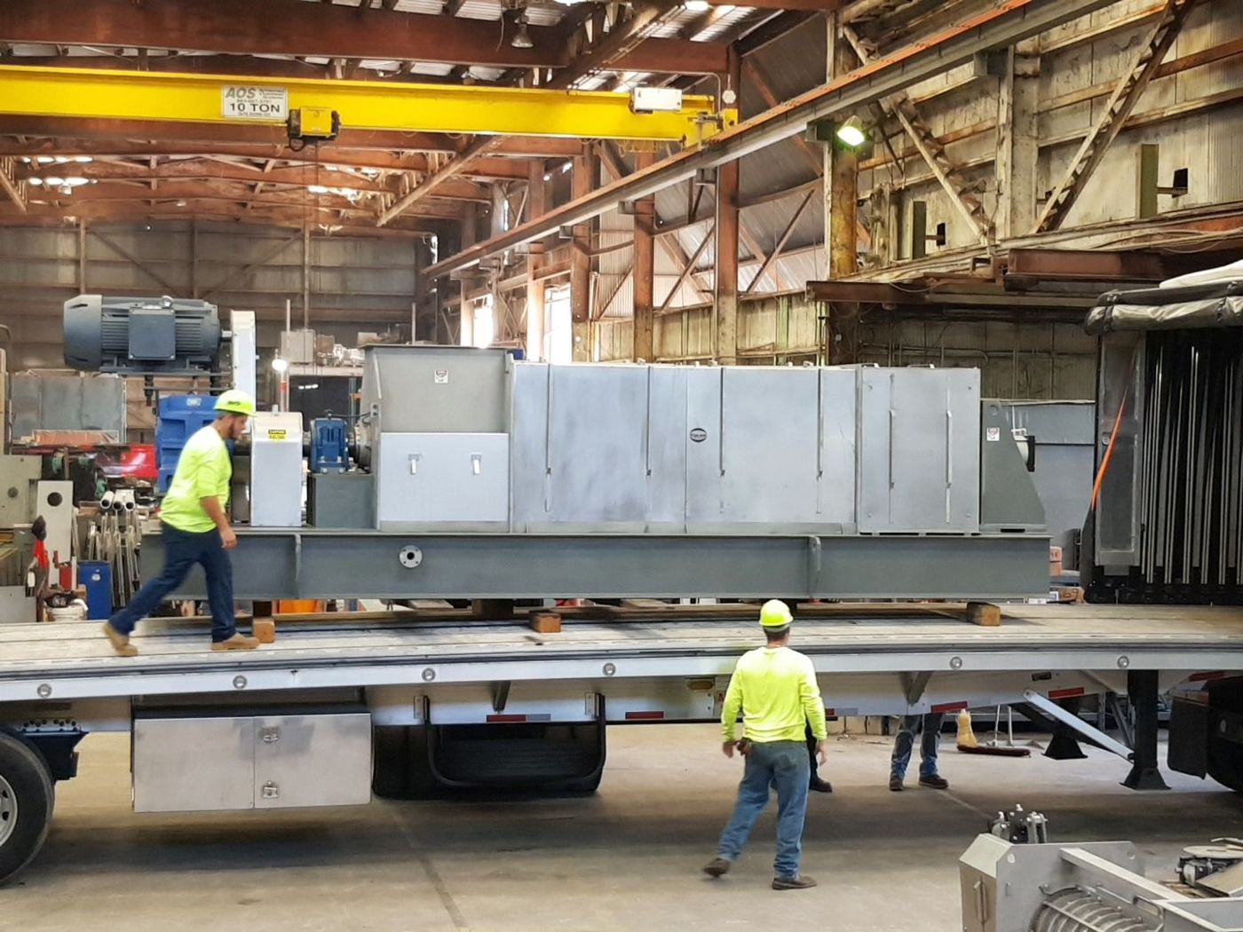 Crew loading a large screw press onto a flatbed truck