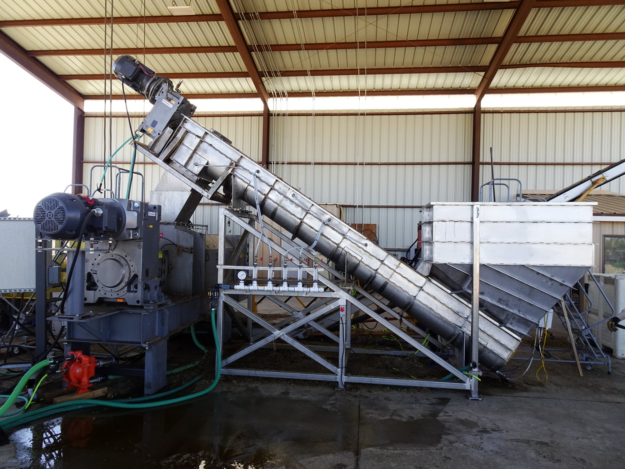 Receiving hopper and incline conveyor feeding a screw press under a covered pad